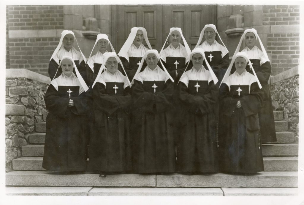 11 femmes habillées de robes noires et blanches, avec des coiffes blanches et des gros crucifix pendant sur la poitrine